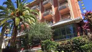 A multi-story hotel with balconies, palm trees, and a clear blue sky. - Hotel Astoria (Bordighera)