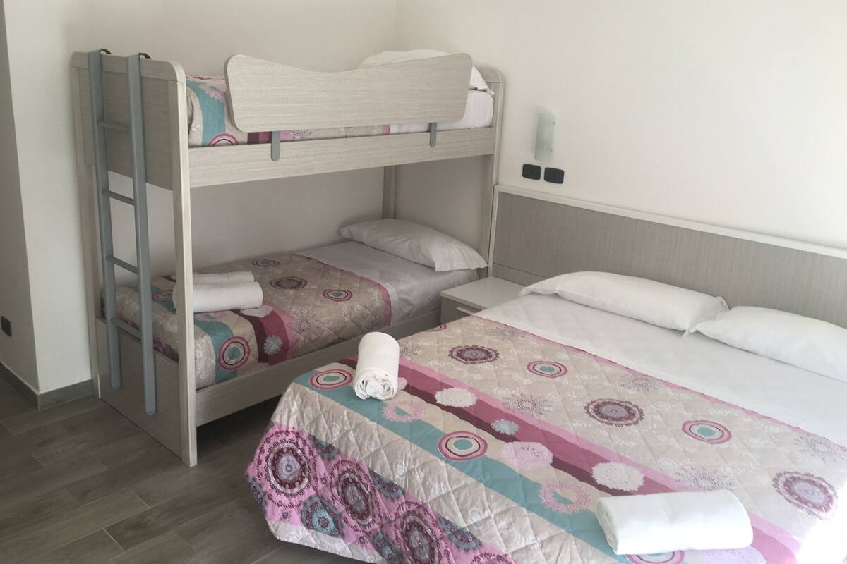 A room with two bunk beds, a small bedside table, and a large bed with a patterned bedspread.