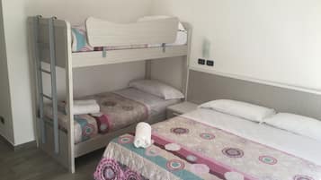 A room with two bunk beds, a small bedside table, and a large bed with a patterned bedspread.
