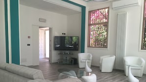 A modern living room with a flat-screen TV, white sofas, and a glass coffee table. - Hotel Astoria (Bordighera)