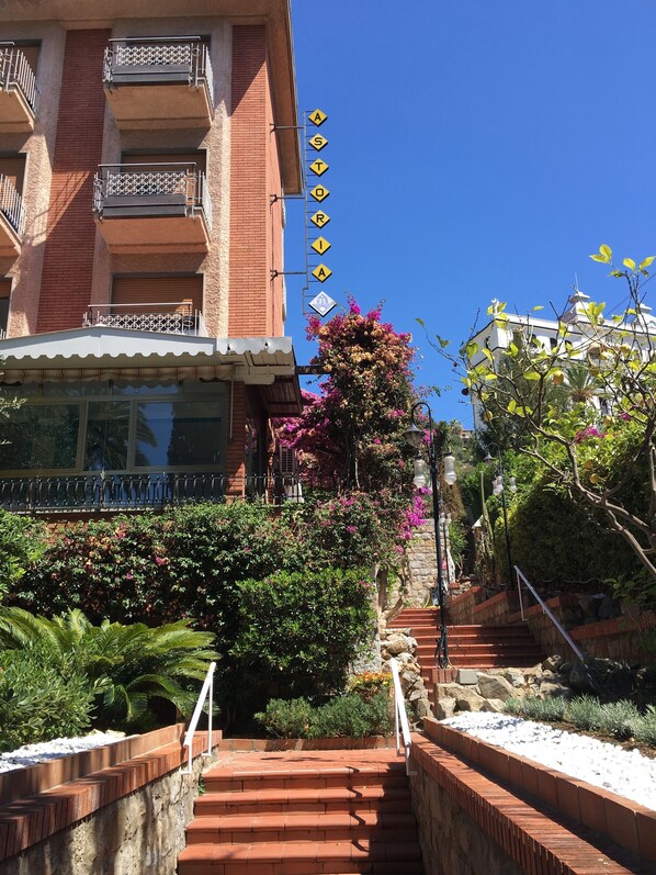 A hotel with a brick facade, multiple balconies with metal railings, and a staircase leading to a lower level.