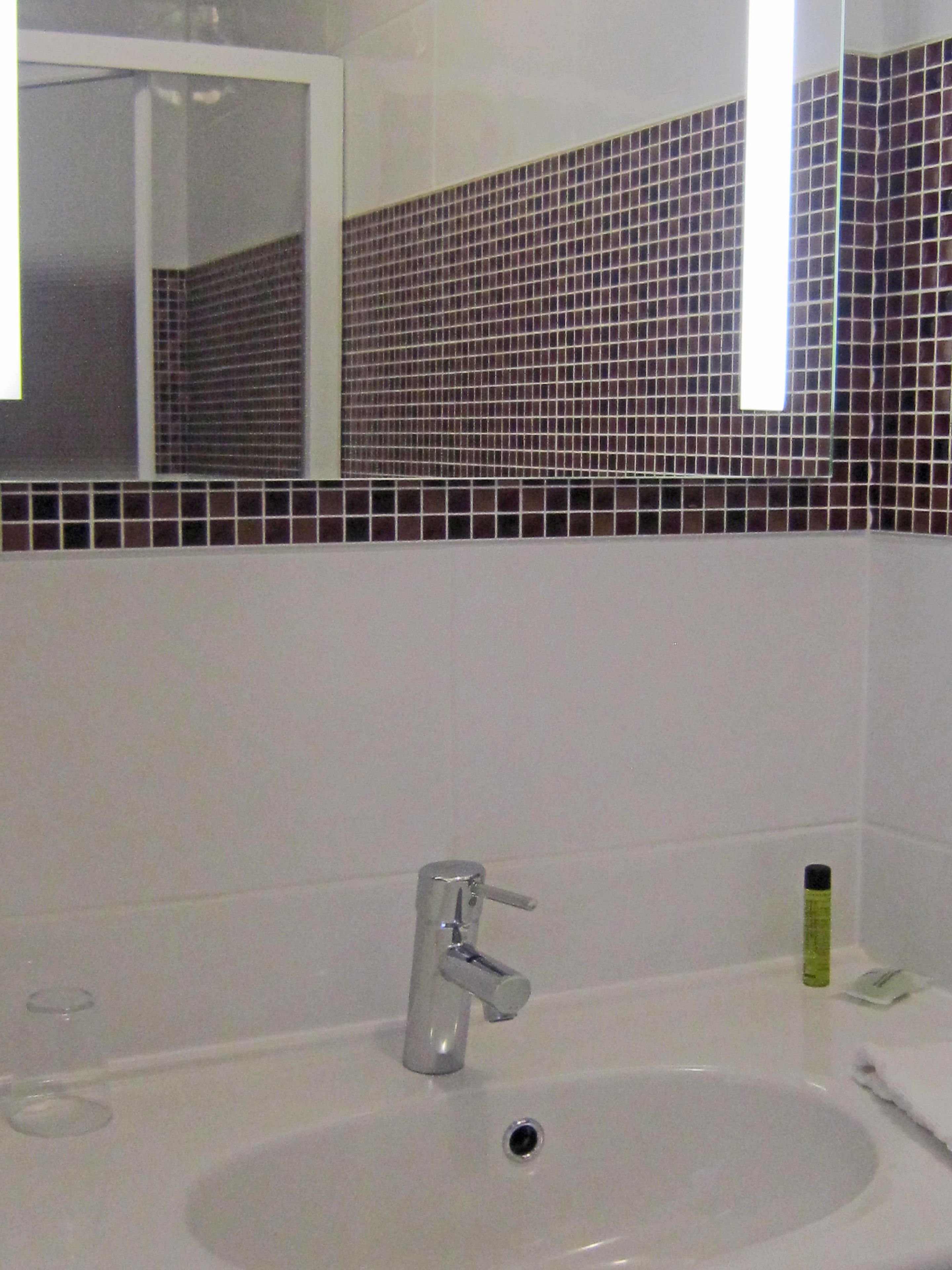 A bathroom with a white sink, a mirror, and a tiled backsplash.