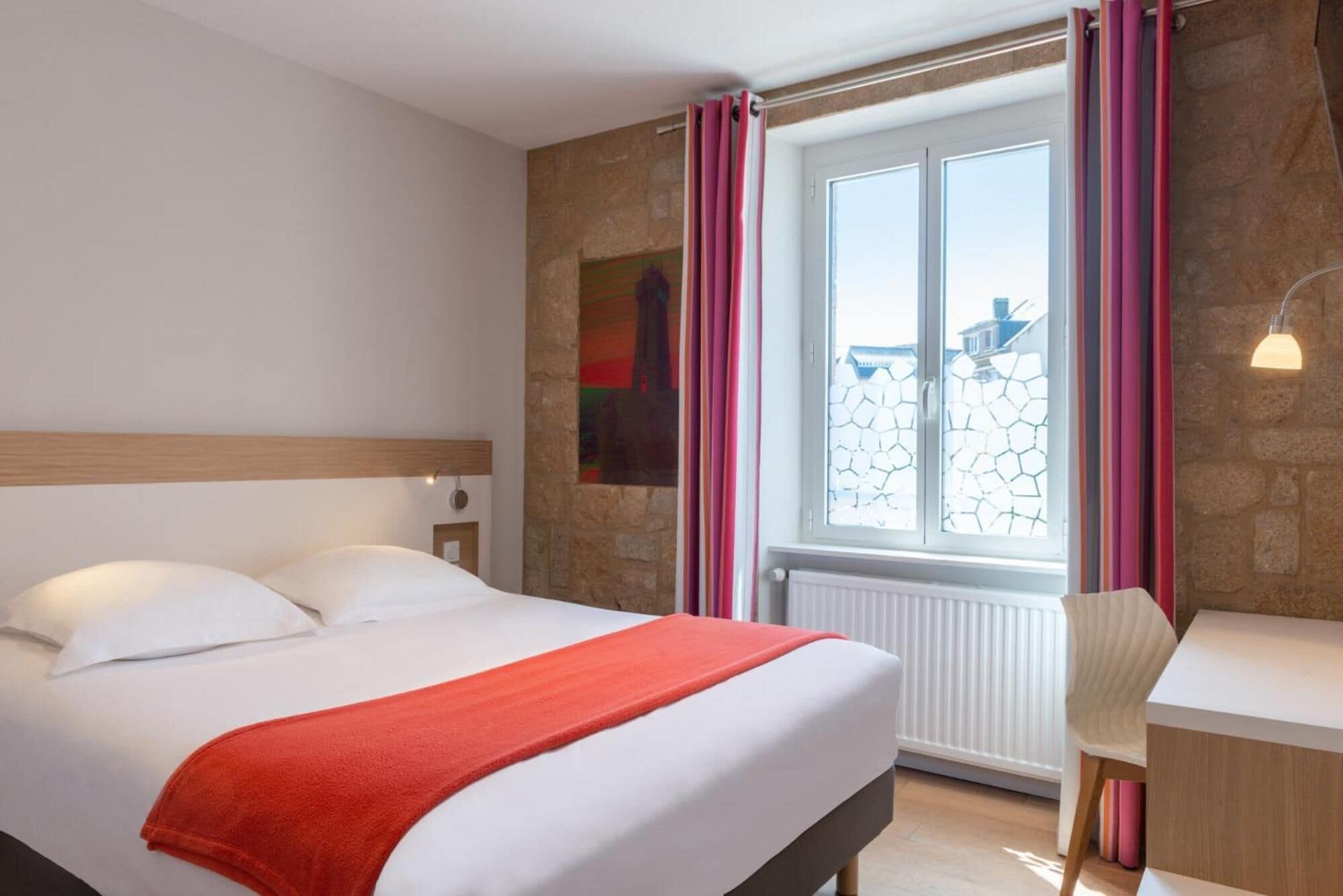 Une chambre d’hôtel avec un lit, un bureau, une chaise et une fenêtre avec des rideaux.