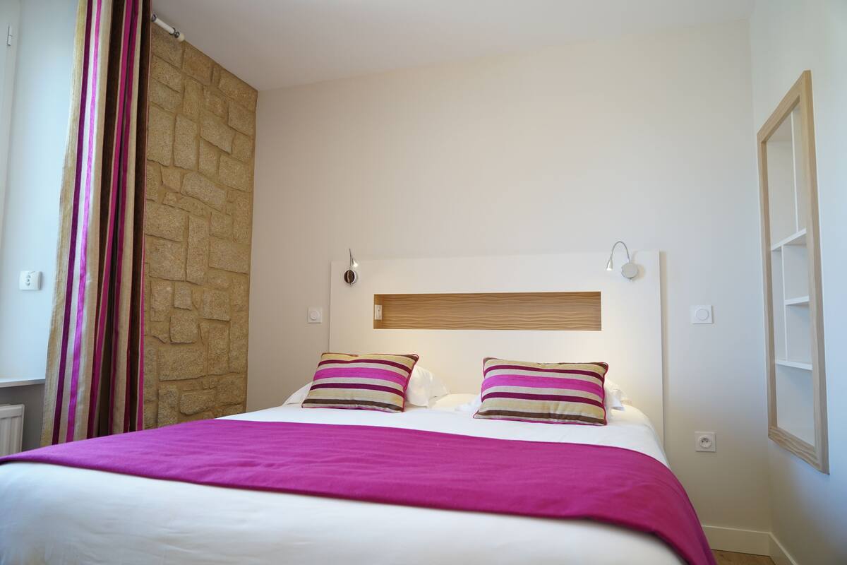 Une chambre à coucher avec un lit, un mur décoratif en pierre, une fenêtre et une table de chevet.