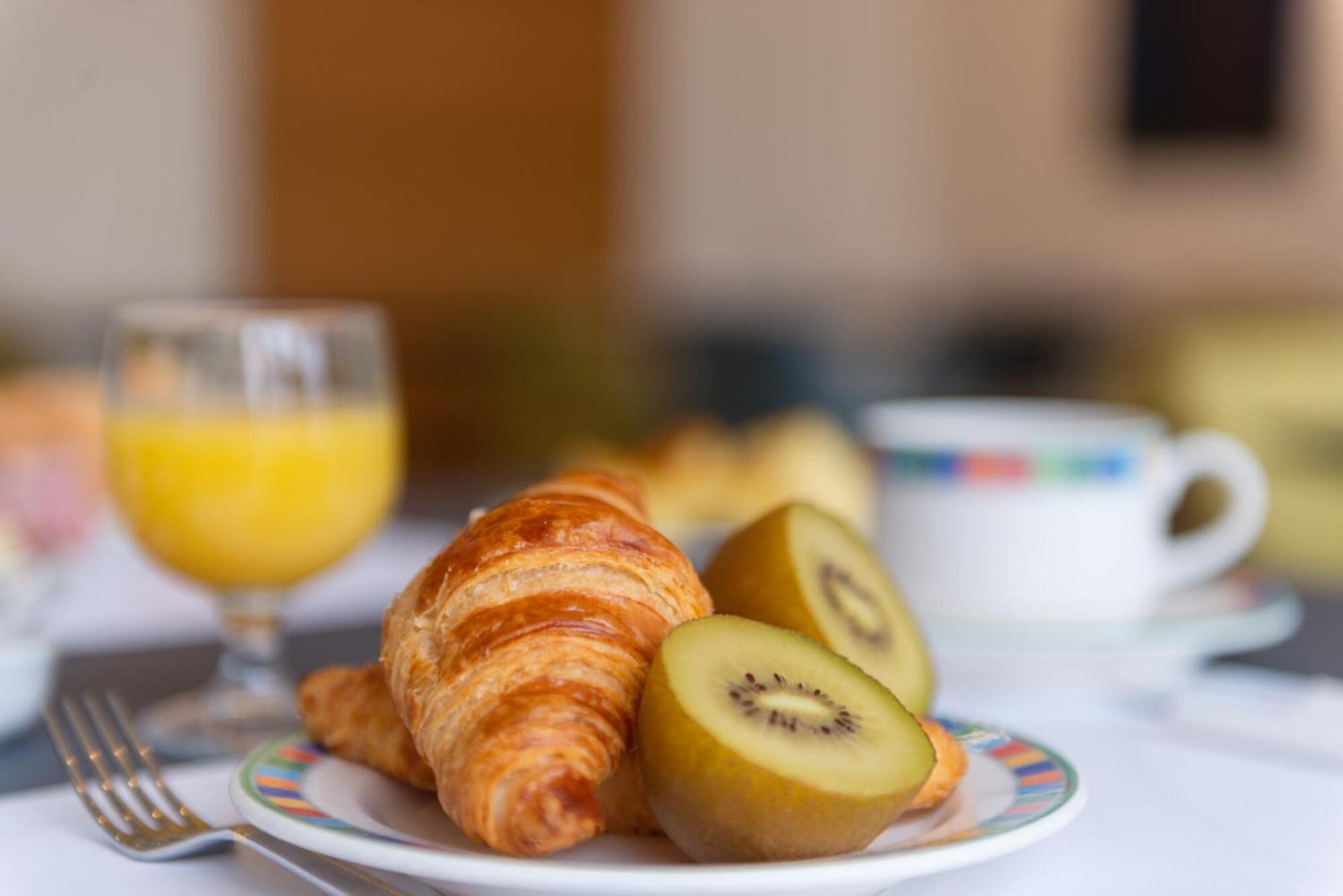 Un croissant, rodajas de kiwi y un vaso de jugo de naranja en un plato.
