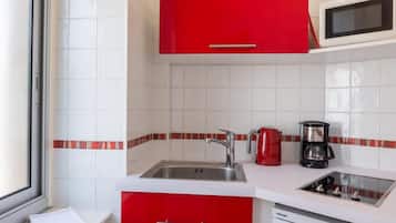 A kitchen with white cabinets, a stainless steel sink, a red kettle, and a coffee maker.