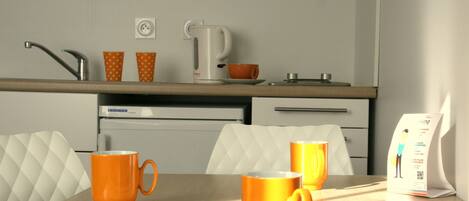 A modern kitchen with a countertop, a kettle, and two orange mugs on a table.
