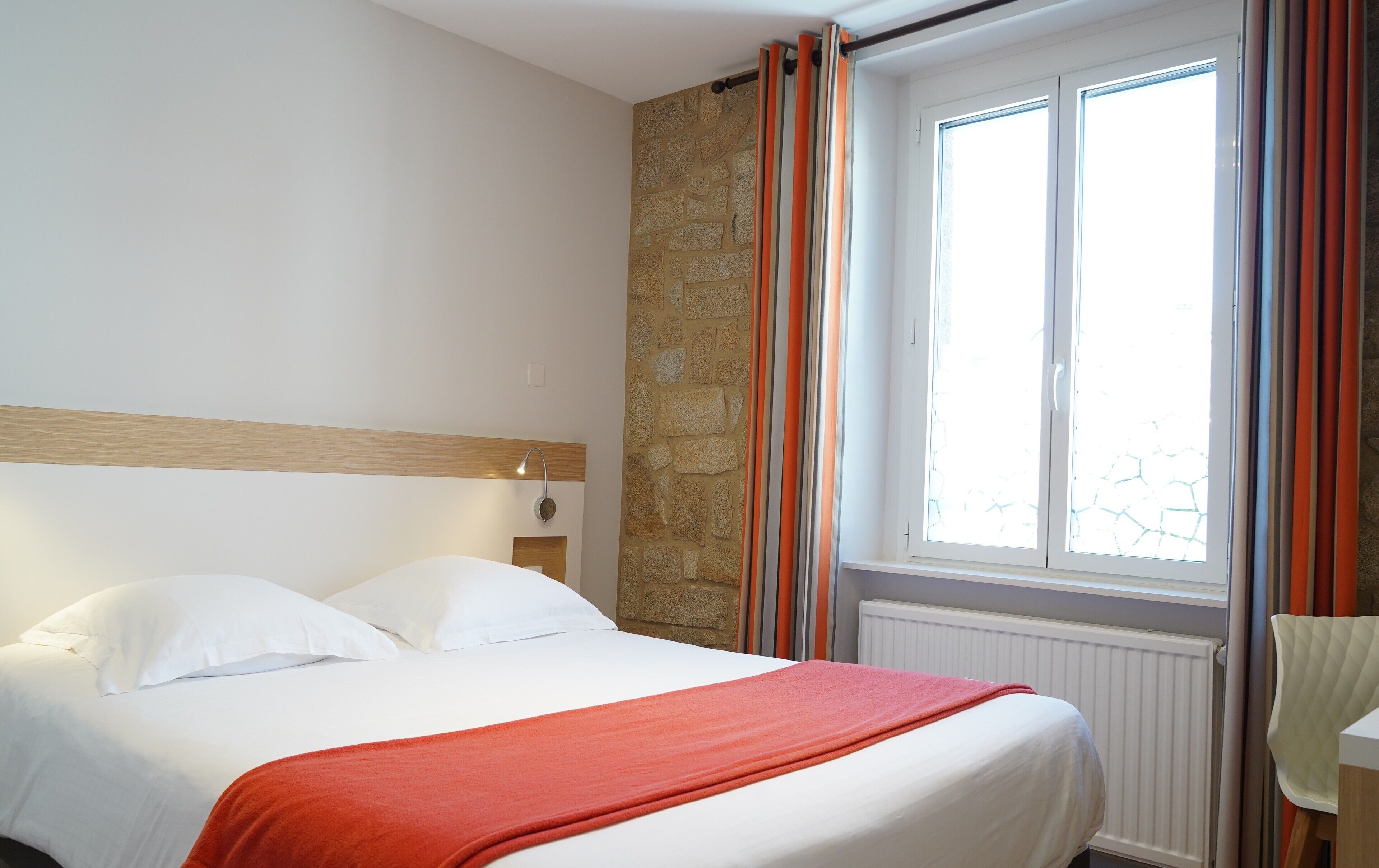 Una habitación de hotel con una cama, un muro de acento de piedra, una ventana con cortinas y un radiador.
