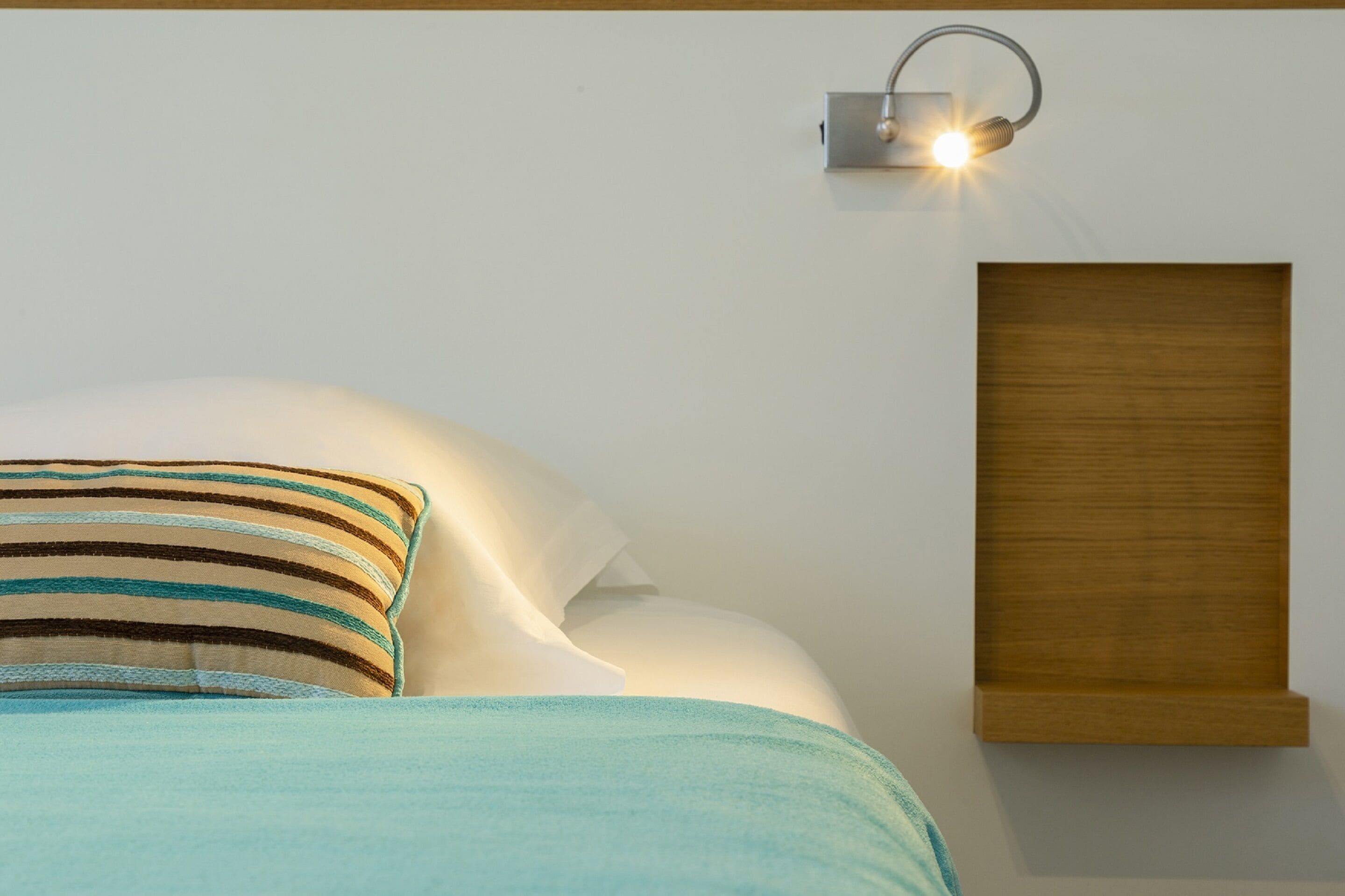 A neatly made bed with striped pillows and a wooden headboard, a wall-mounted light fixture, and a wooden panel on the wall.