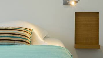 A neatly made bed with striped pillows and a wooden headboard, a wall-mounted light fixture, and a wooden panel on the wall.