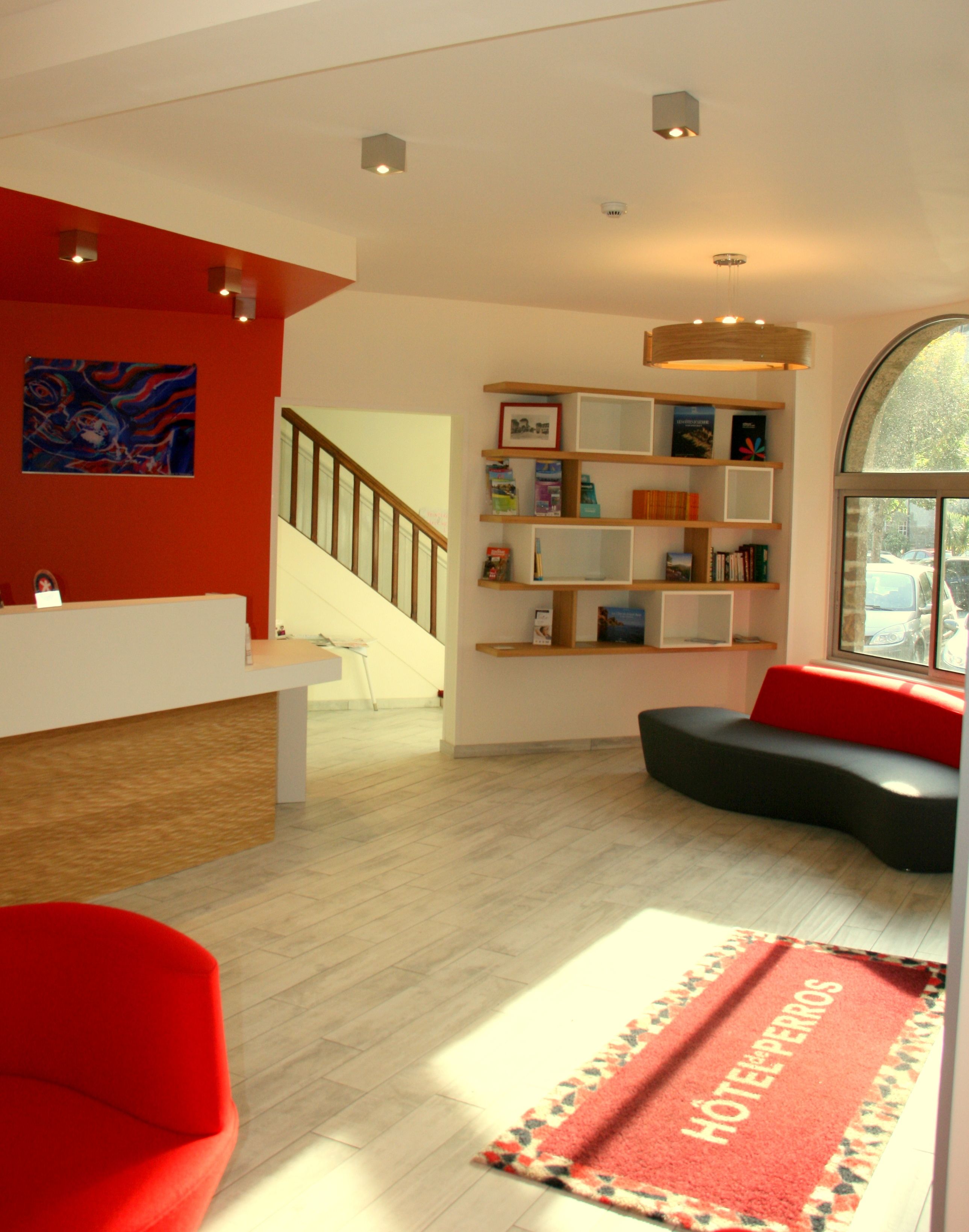 A modern hotel lobby with a staircase, a red sofa, a bookshelf, and a red carpet with "HOTEL PERROS" text.