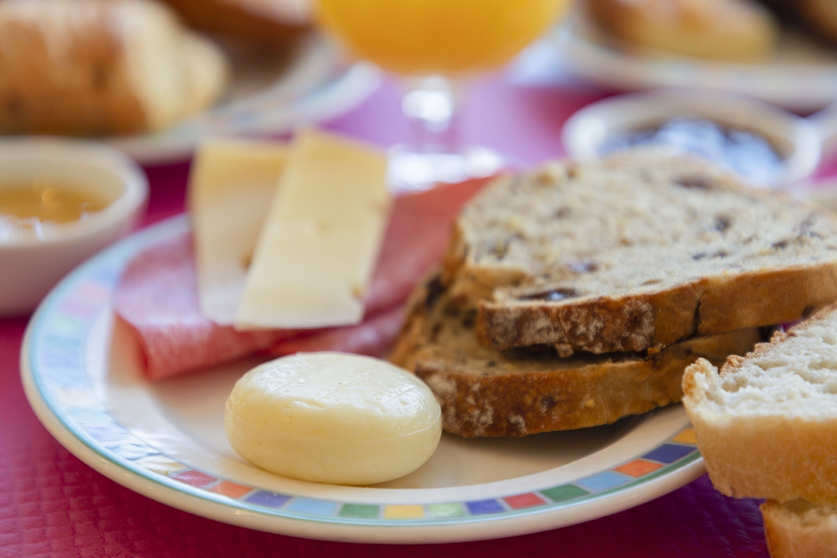 A plate with slices of bread, a round cheese, and a glass of orange juice.