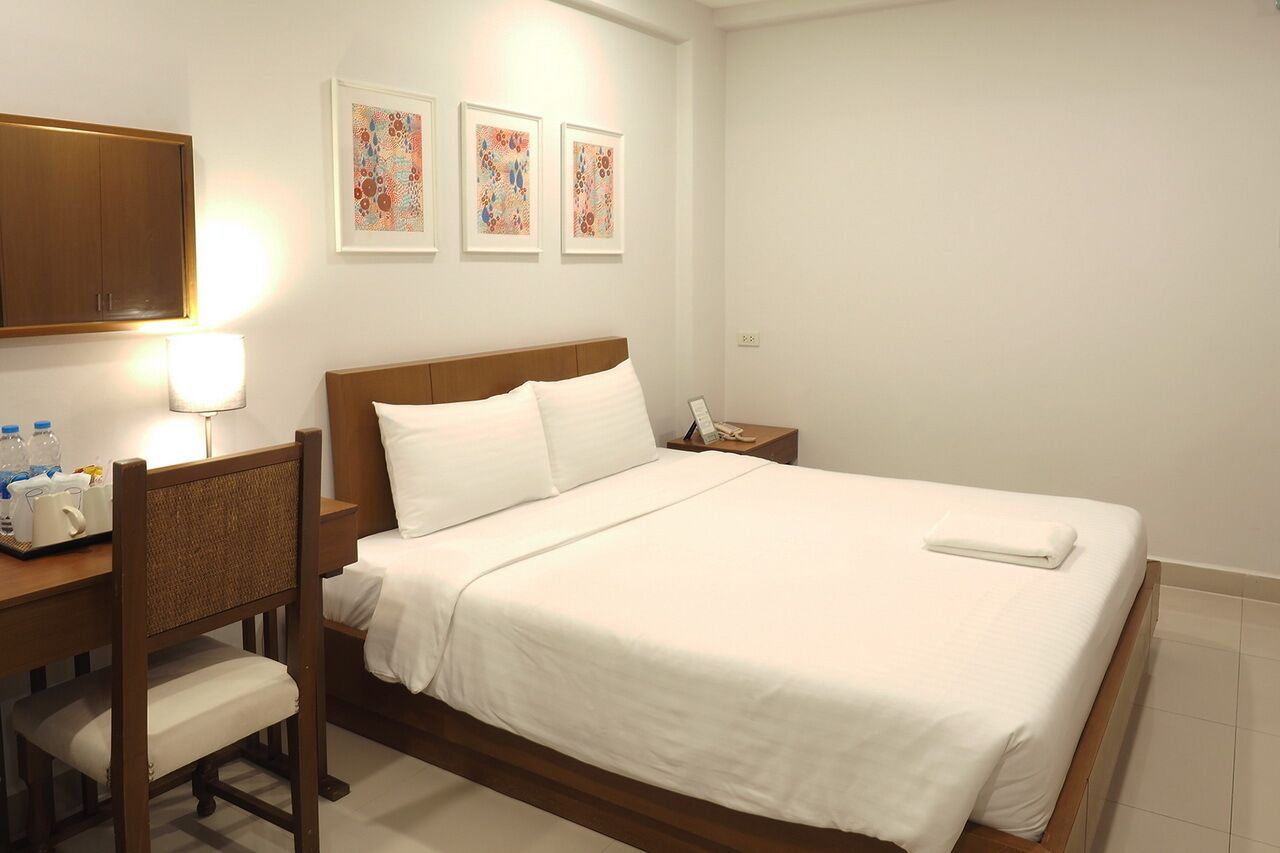 A hotel room with a bed, a desk with a lamp, a chair, and a nightstand.