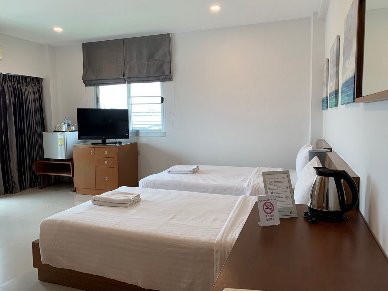 Camera d'albergo con due letti, televisione, minibar, macchina del caffè e cartello 'area fumatori'.