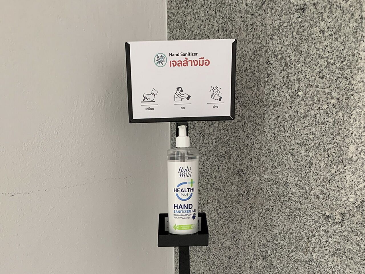 Een handdesinfecteerder aan een muur bevestigd, met een bord erboven.