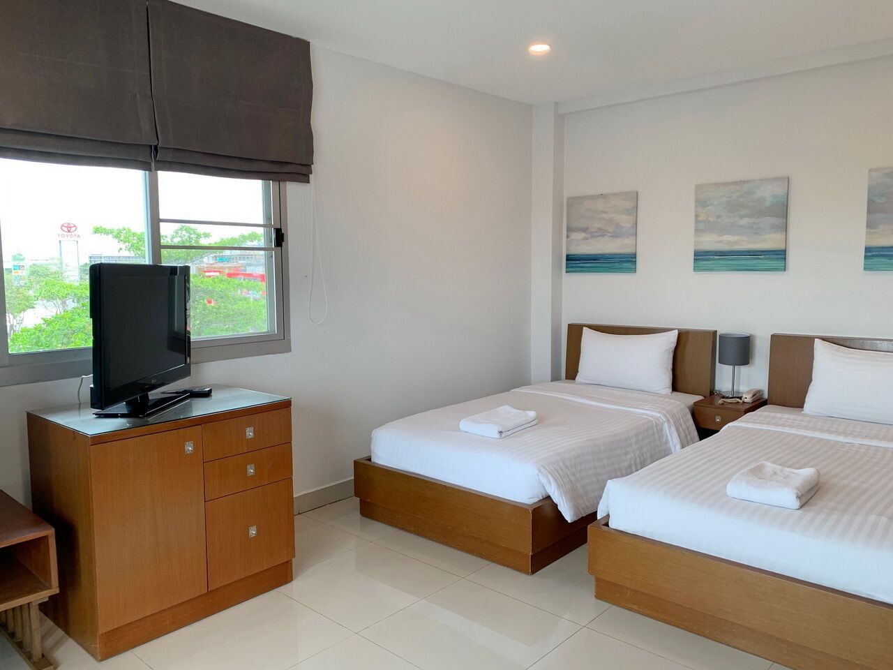 A hotel room with two beds, a TV on a wooden cabinet, and artwork on the wall.