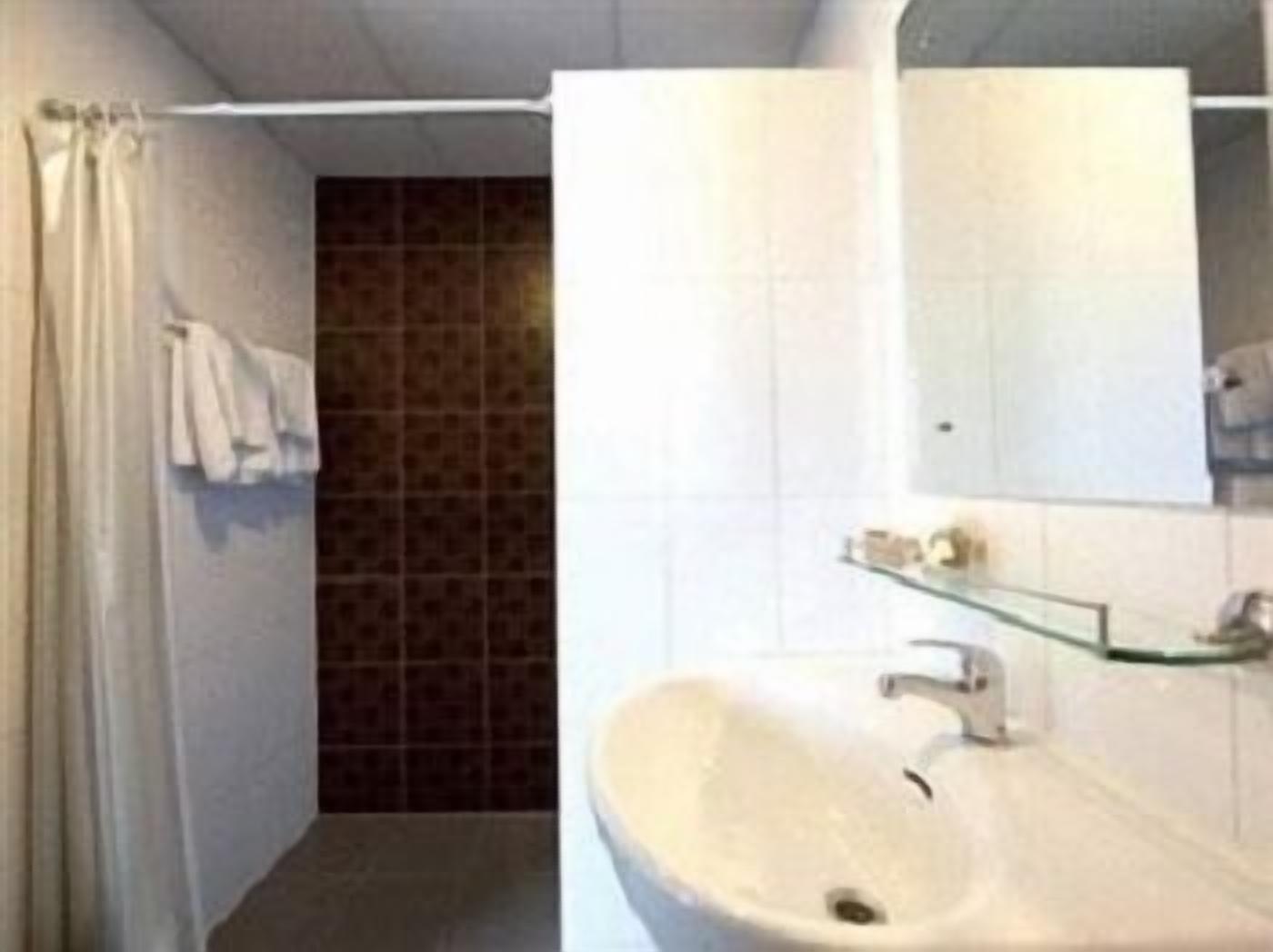 A bathroom with a white sink, a glass shelf, a mirror, and a shower curtain.