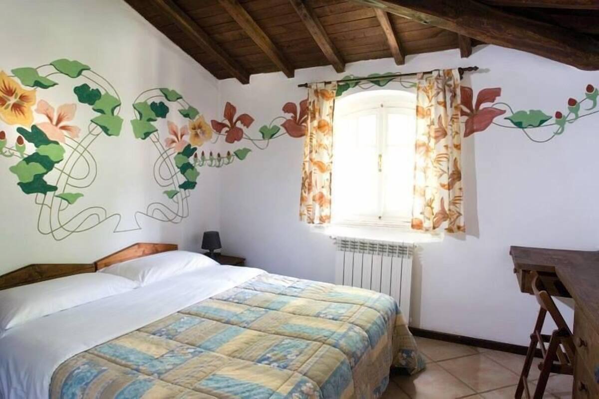 Un dormitorio con cama, ventana con cortinas florales y radiador.
