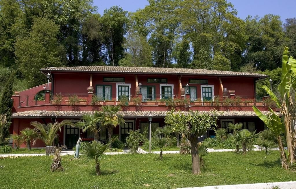 A two-story building with a red facade, multiple windows with green shutters, and a tiled roof.