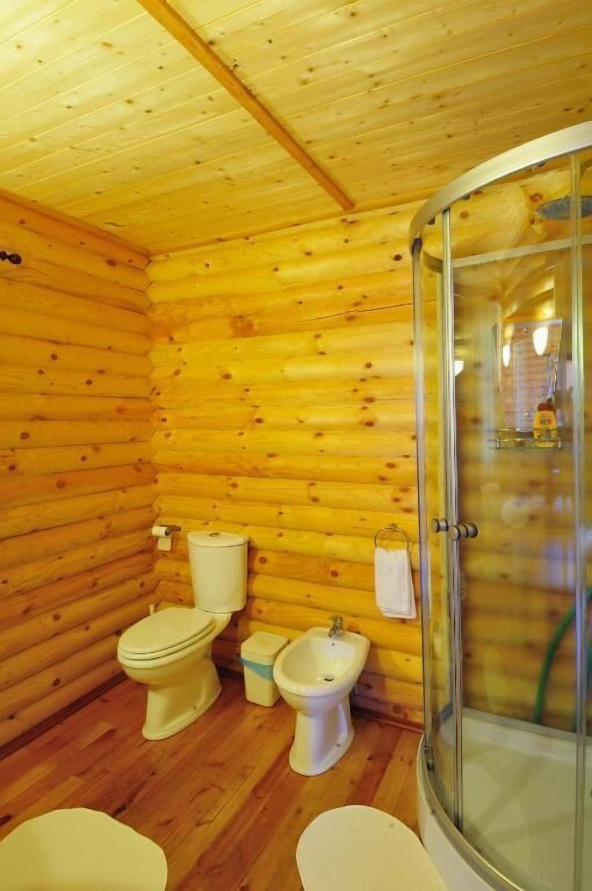 Baño de cabaña de madera con ducha, dos inodoros y un bidé.