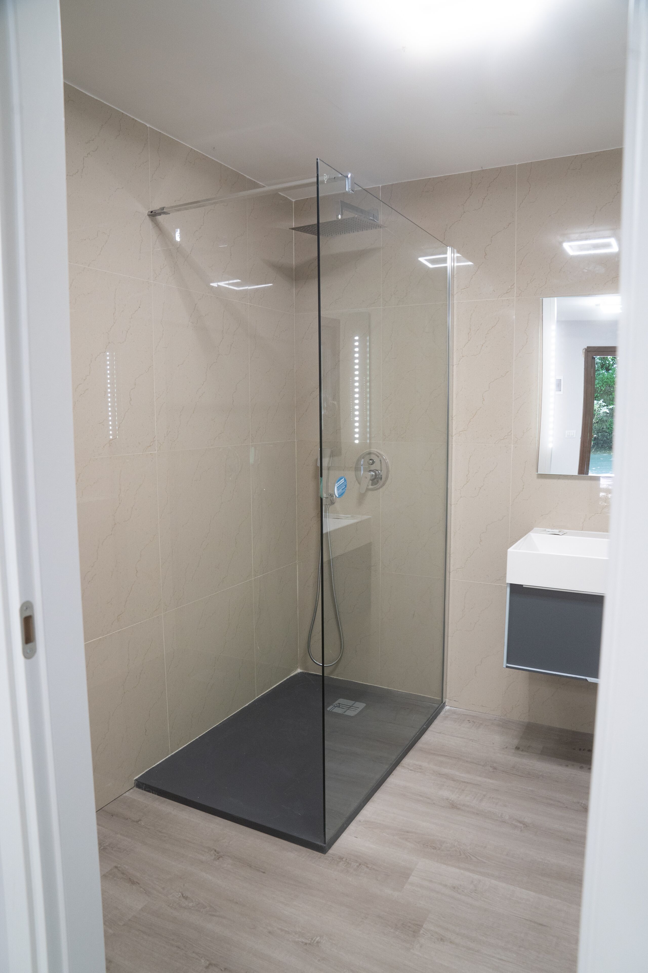 A modern bathroom with a glass-enclosed shower, a white sink, and a mirror above it.
