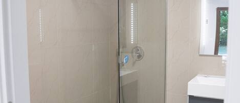 Une salle de bain moderne avec une douche à parois de verre, un lavabo blanc et un miroir au-dessus.
