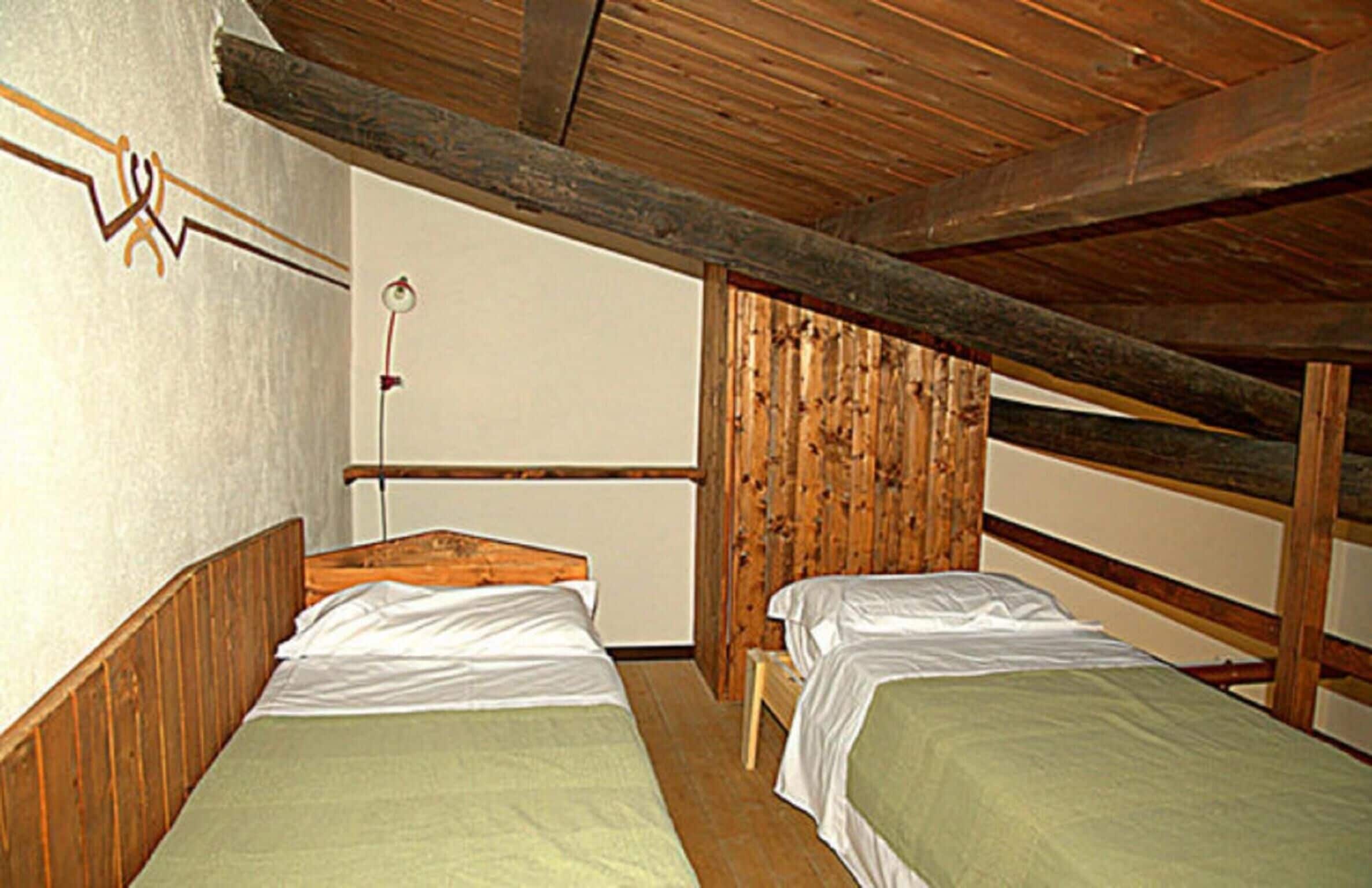 A small, rustic room with two wooden bunk beds, a wooden ceiling, and a simple wall-mounted light fixture.