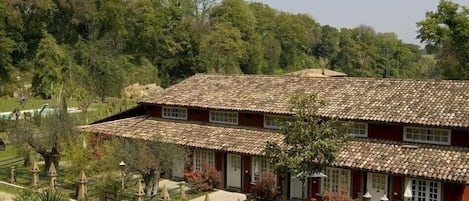 A two-story building with a tiled roof, surrounded by a garden with various plants and a pathway leading to the entrance.