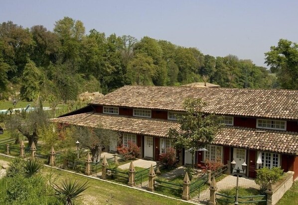 A two-story building with a tiled roof, surrounded by a garden with various plants and a pathway leading to the entrance. - Veio Residence Resort (Rome)