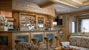 A wooden bar area with a bartender, bar stools, and shelves of liquor bottles. - Cristallo Hotel Residence (Bormio)