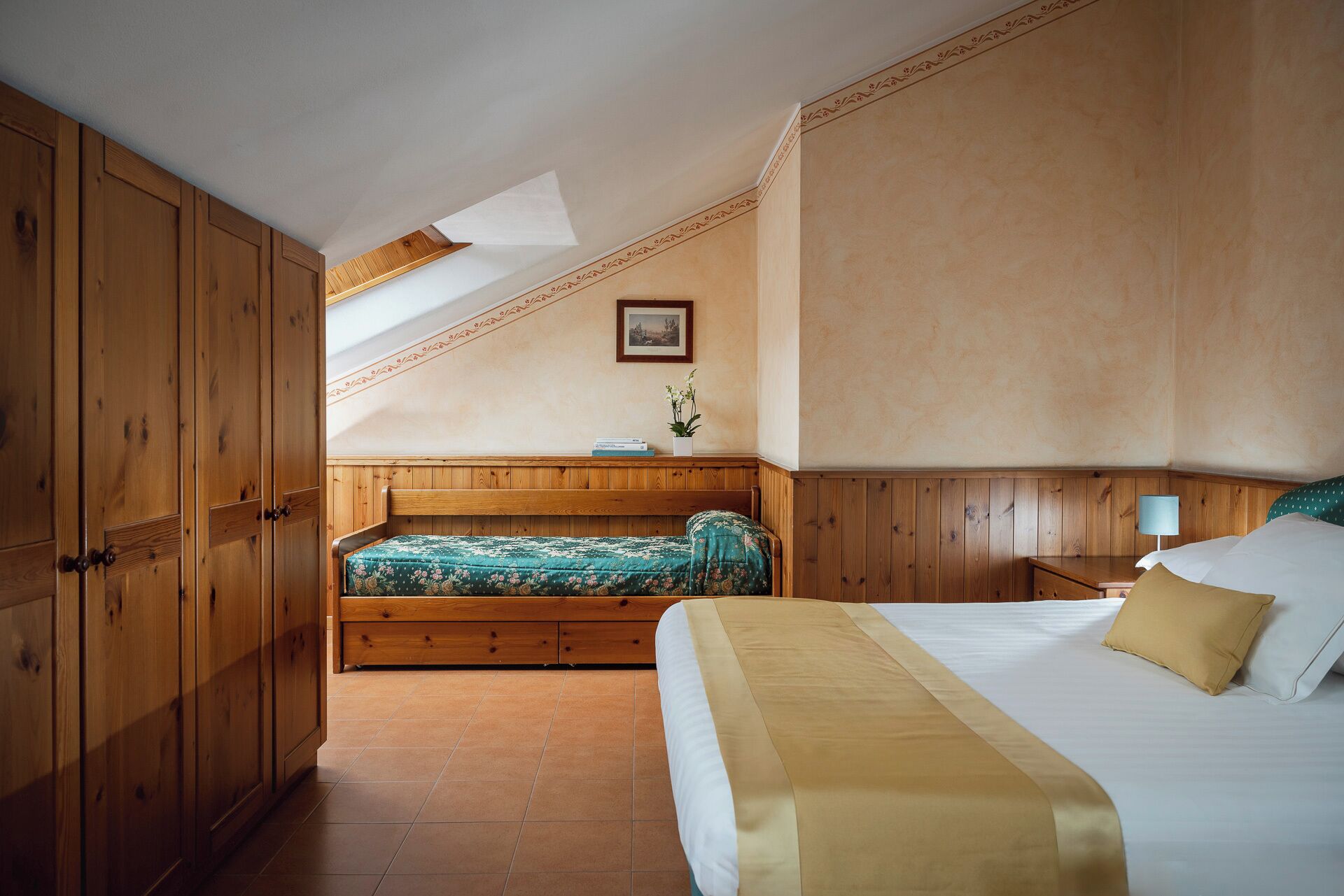 A bedroom with a large bed, a smaller bed, wooden paneling, a skylight, and a framed picture on the wall.