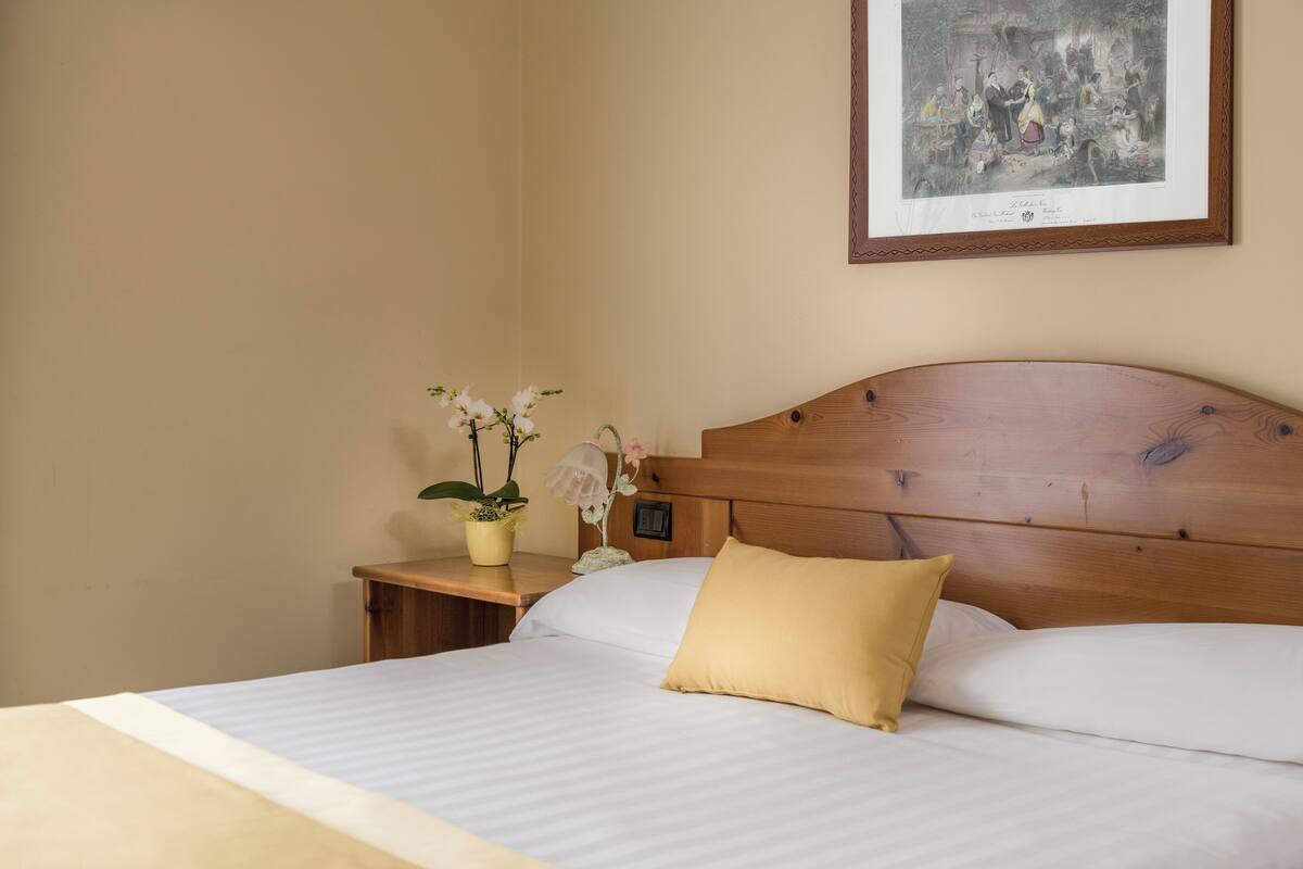 A neatly made bed with white and yellow pillows, a wooden headboard, and a framed picture on the wall.