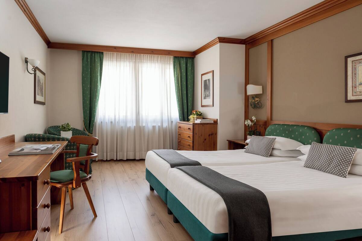 A hotel room with a bed, a desk, a chair, a dresser, and a window with curtains.
