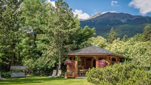 A wooden gazebo with a tiled roof surrounded by lush greenery and a mountain in the background. - Cristallo Hotel Residence (Bormio)