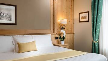 Un letto rifatto con lenzuola bianche e una coperta beige, una lampada da comodino e un quadro appeso al muro.