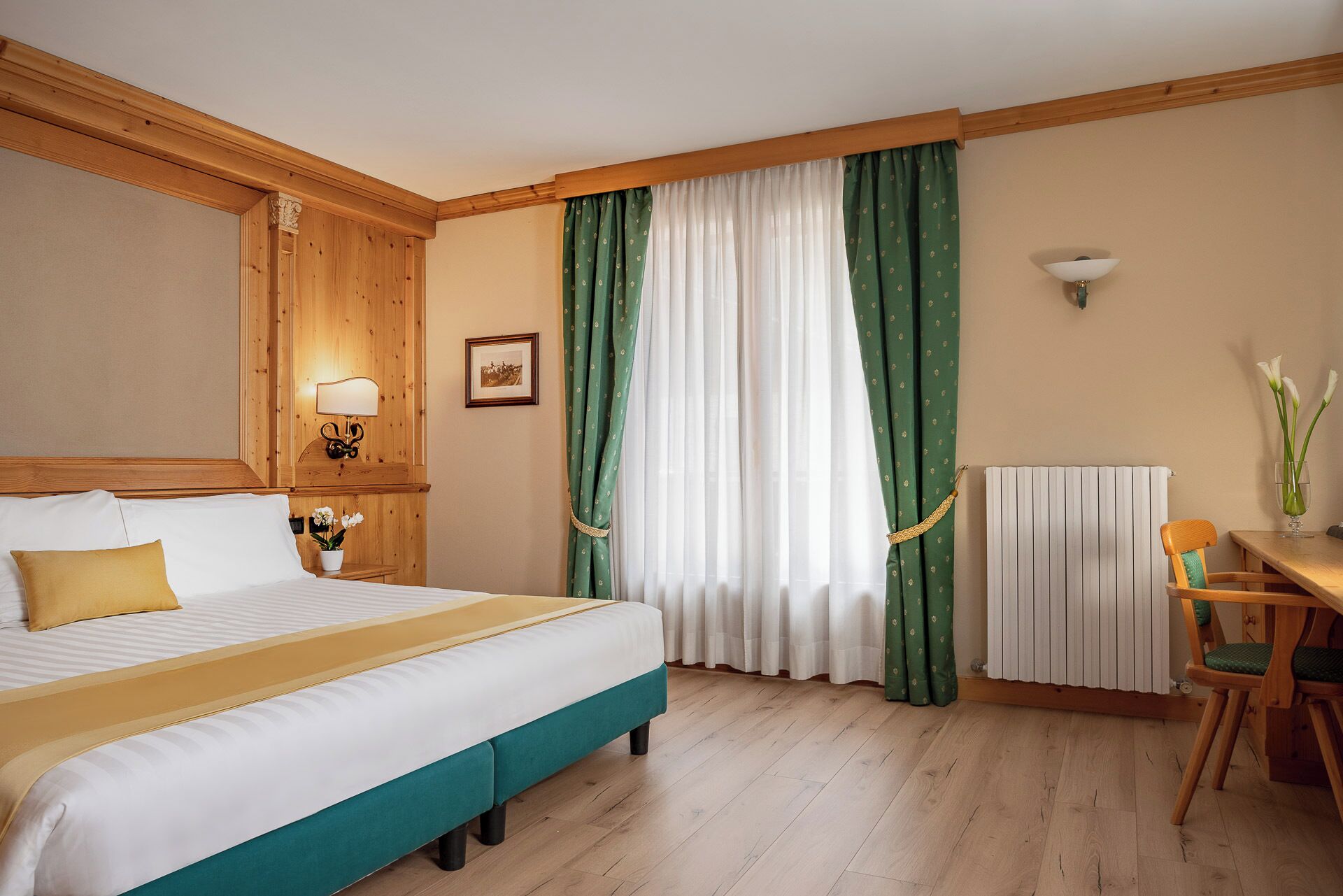 Ein Hotelzimmer mit Bett, Schreibtisch, Stuhl, Lampe, einem Bild an der Wand und einem Fenster mit Vorhängen.