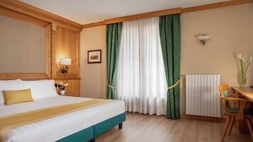 Ein Hotelzimmer mit Bett, Schreibtisch, Stuhl, Lampe, einem Bild an der Wand und einem Fenster mit Vorhängen.