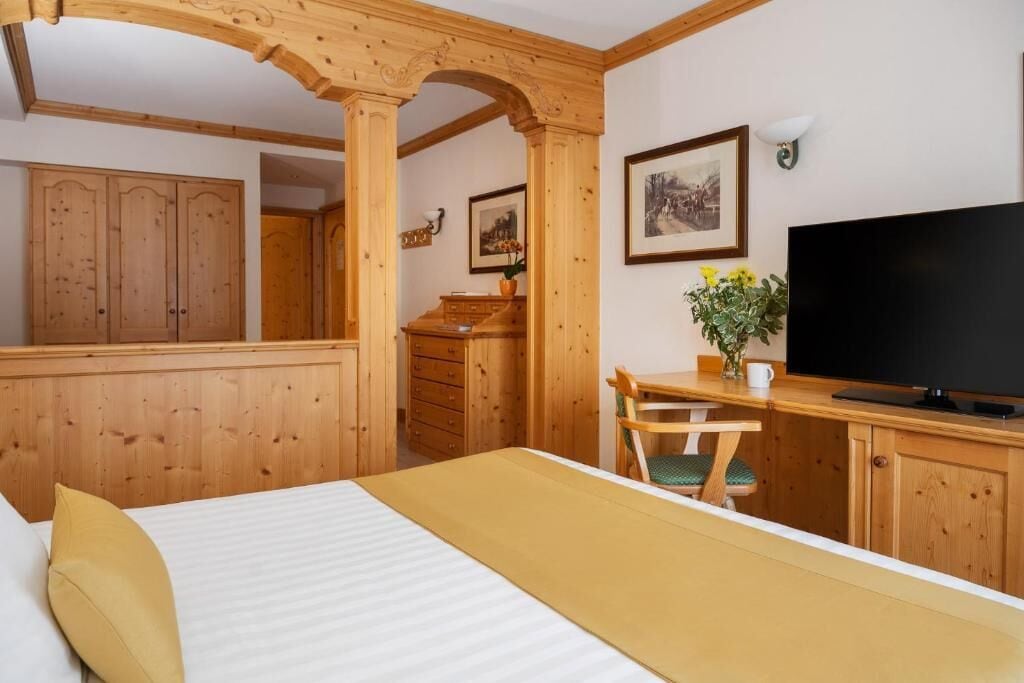 Habitación de hotel con muebles de madera, una cama, un escritorio con silla, un televisor y un cuadro en la pared.