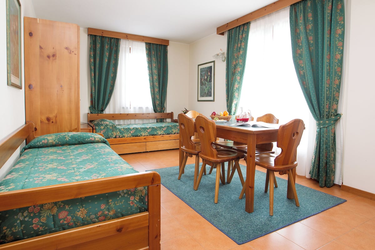 A room with a bed, a dining table with chairs, and a window with curtains.