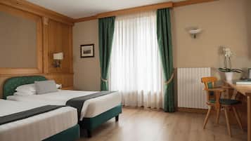 Habitación de hotel con dos camas, un escritorio con una silla, un radiador y un cuadro en la pared.