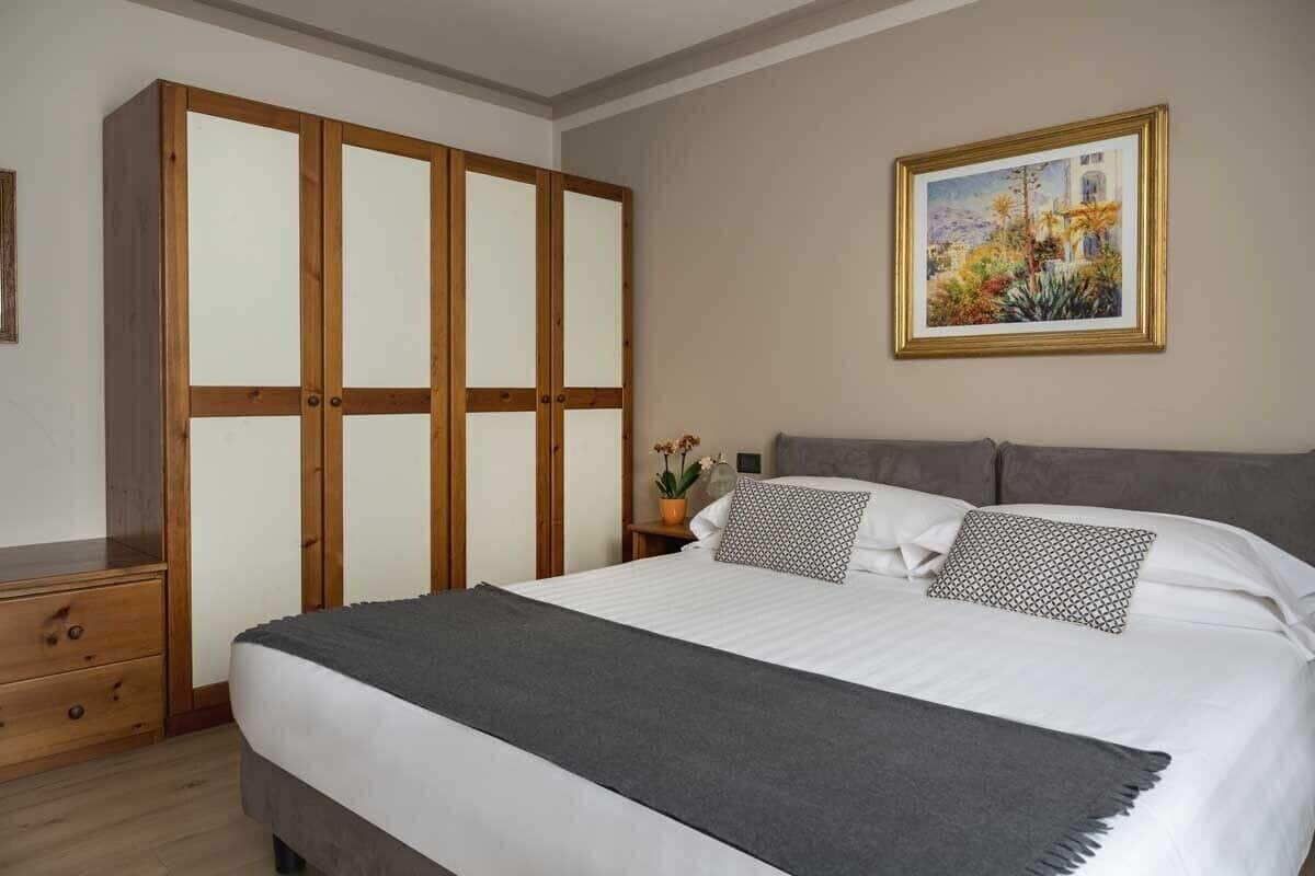 A bedroom with a bed, a wardrobe, a nightstand, and a framed painting on the wall.