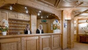 A wooden reception desk with a digital clock, potted orchids, and framed pictures on the wall. - Cristallo Hotel Residence (Bormio)