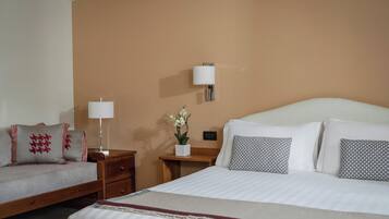 Una habitación de hotel con una cama, una mesita de noche, una lámpara y un velador.