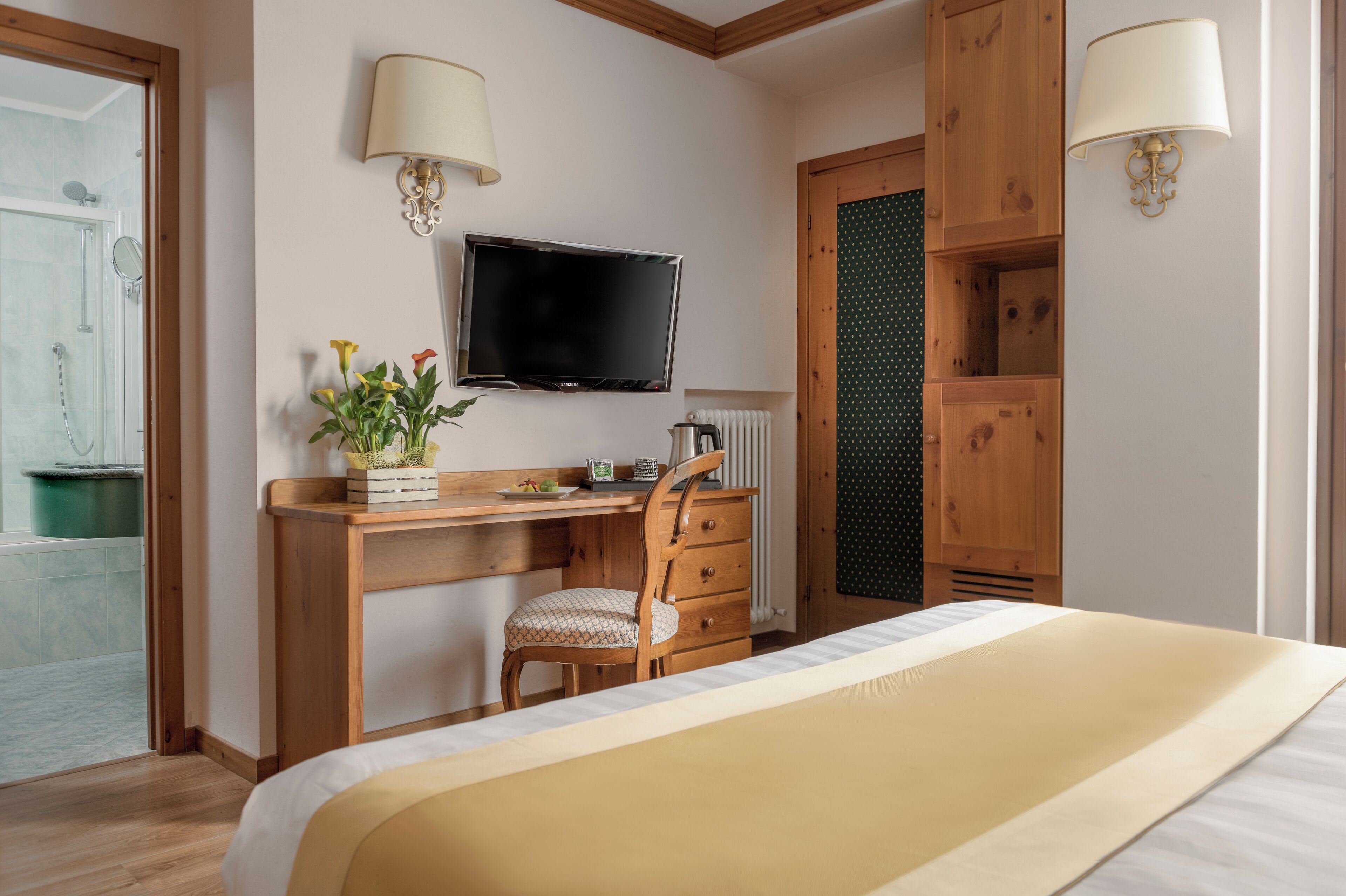 Une chambre d’hôtel avec un bureau en bois, une chaise, un lit, une télévision et une salle de bain visible à travers une porte ouverte.