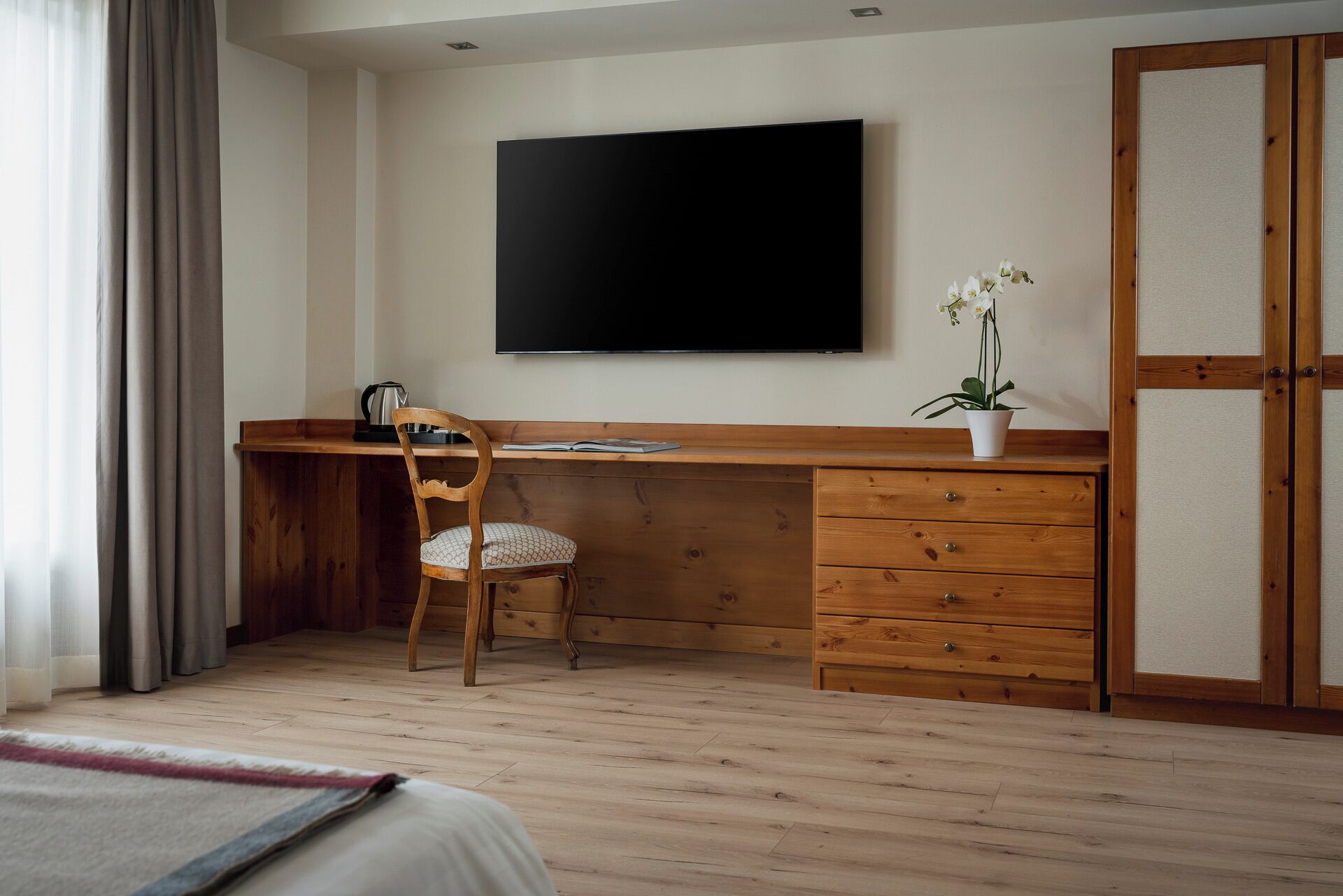A room with a wooden desk, a chair, a flat-screen TV, a potted plant, and a wardrobe.
