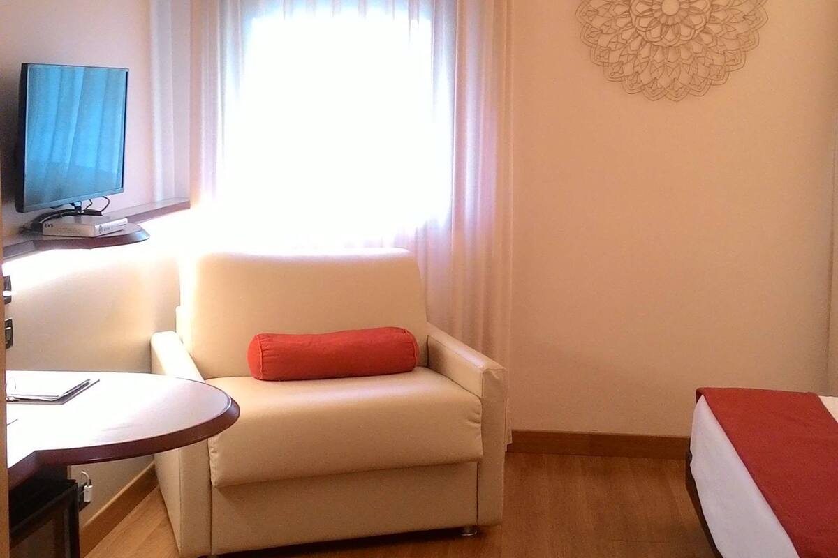 A hotel room with a sofa, a bed, a desk with a computer, and a wall with a decorative pattern.