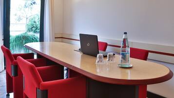 Ein Konferenzraum mit einem langen Tisch, roten Stühlen, einem Laptop und einer Wasserflasche.