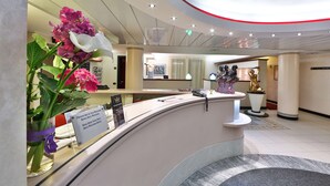 A hotel reception area with a curved reception desk, a signboard, a vase with flowers, and a statue. - Best Western Hotel Solaf (Medolago)