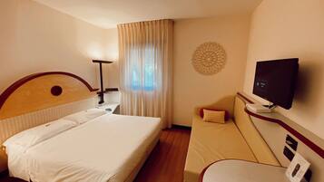 A hotel room with a bed, a sofa, a TV, and a desk with a computer.