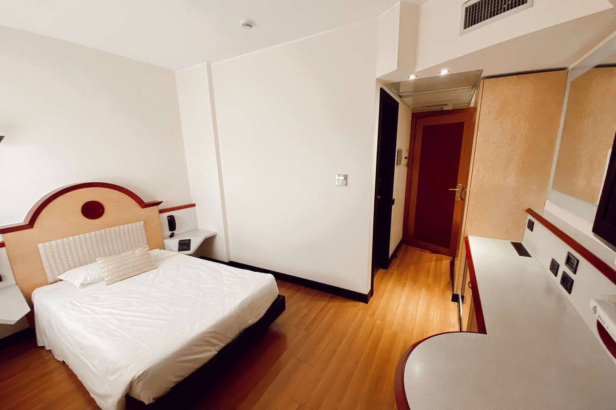 A hotel room with a bed, bedside table, and a small desk.